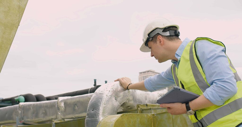 Engineer inspecting insulated pipelines at an industrial site with a digital tablet.